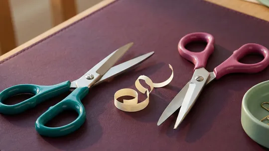 Left-handed scissors in teal beside right-handed scissors in magenta on a plum surface, representing neuroaffirming practice of adapting tools to fit the people using them.