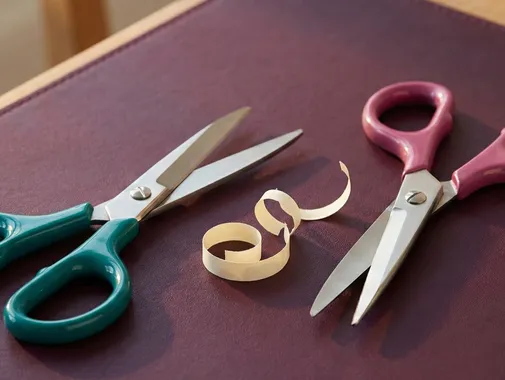 Left-handed scissors in teal beside right-handed scissors in magenta on a plum surface, representing neuroaffirming practice of adapting tools to fit the people using them.