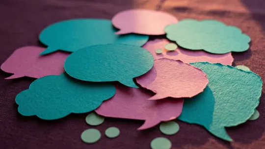 Teal and magenta paper speech bubbles and thought clouds layered together, representing behaviour as an alternative language when words aren't available.
